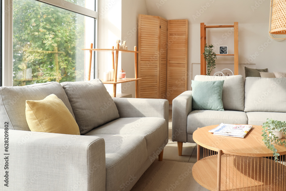 Interior of light living room with cozy grey sofas and wooden coffee table