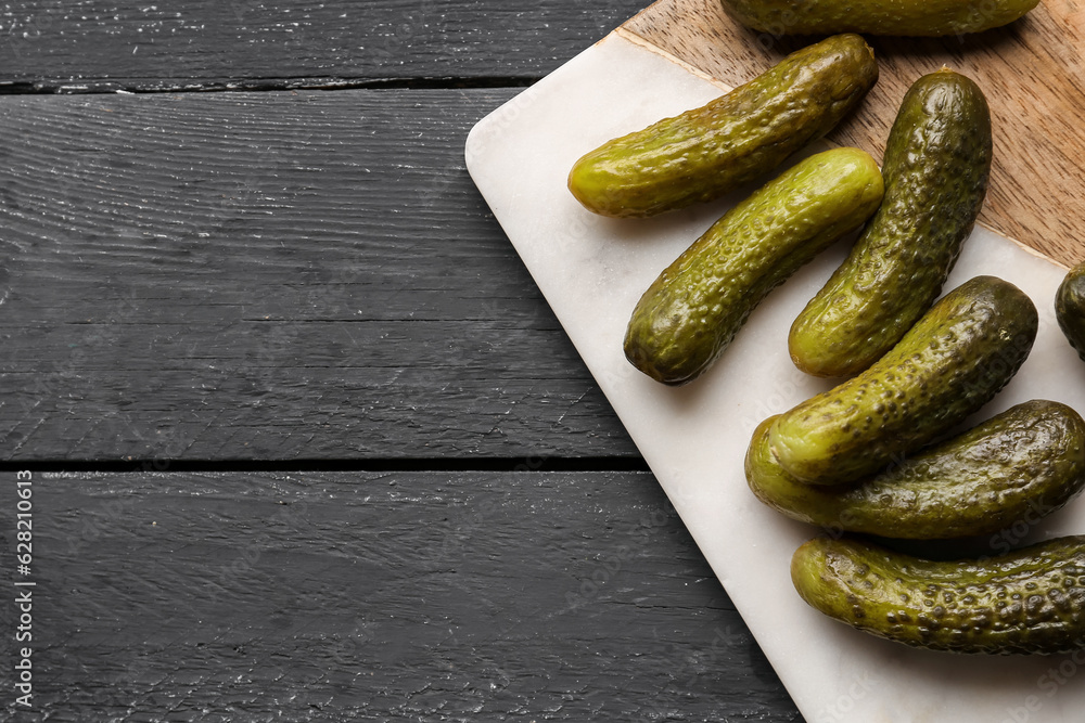 Board with pickled cucumbers on black wooden background