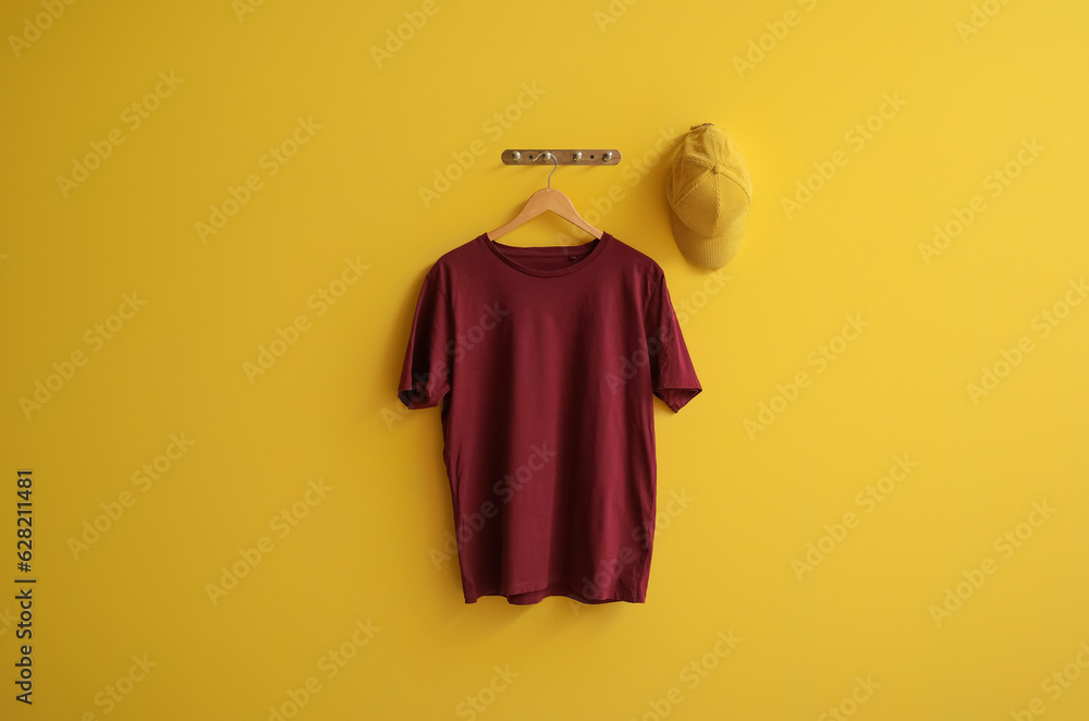 Stylish red t-shirt and cap hanging on yellow background