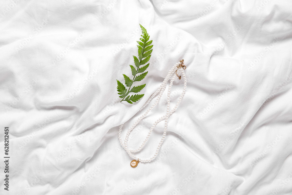 Beautiful pearl necklaces with plant leaves on white cloth