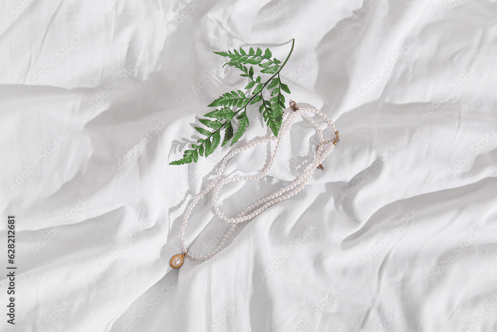 Beautiful pearl necklaces with plant branch on white cloth