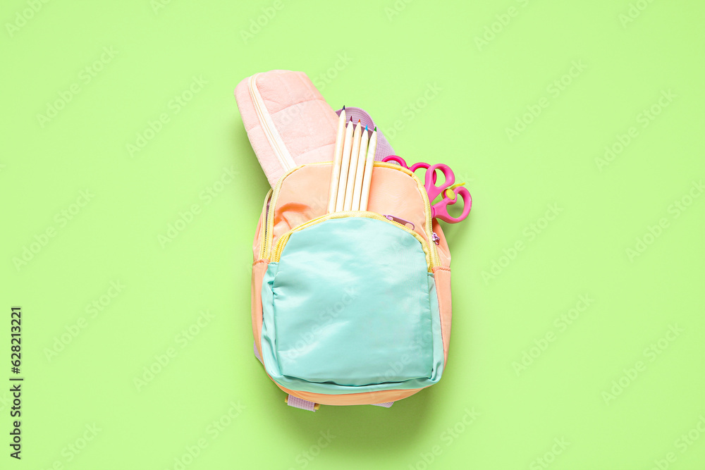 Color school backpack with different stationery on green background