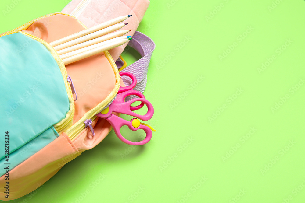 Color school backpack with different stationery on green background