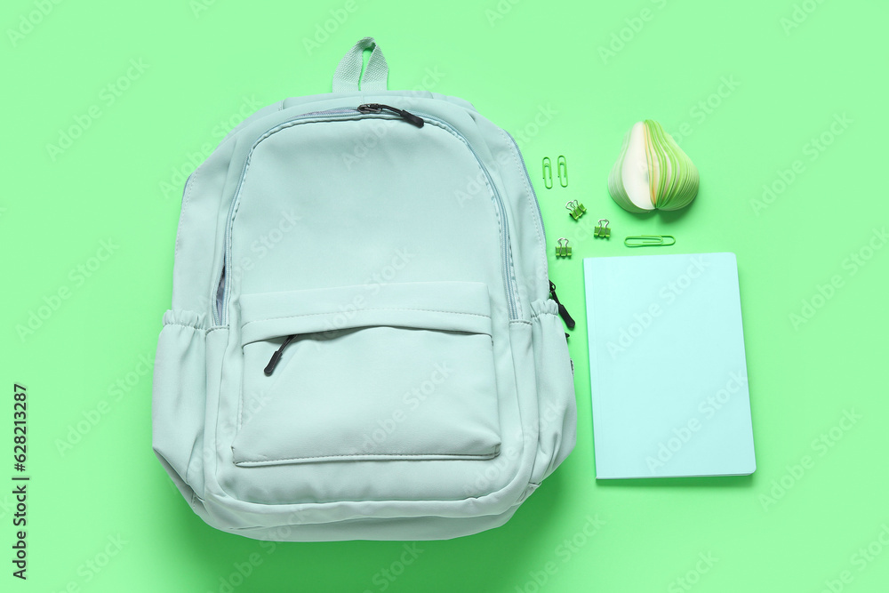 Stylish school backpack with different stationery on green background