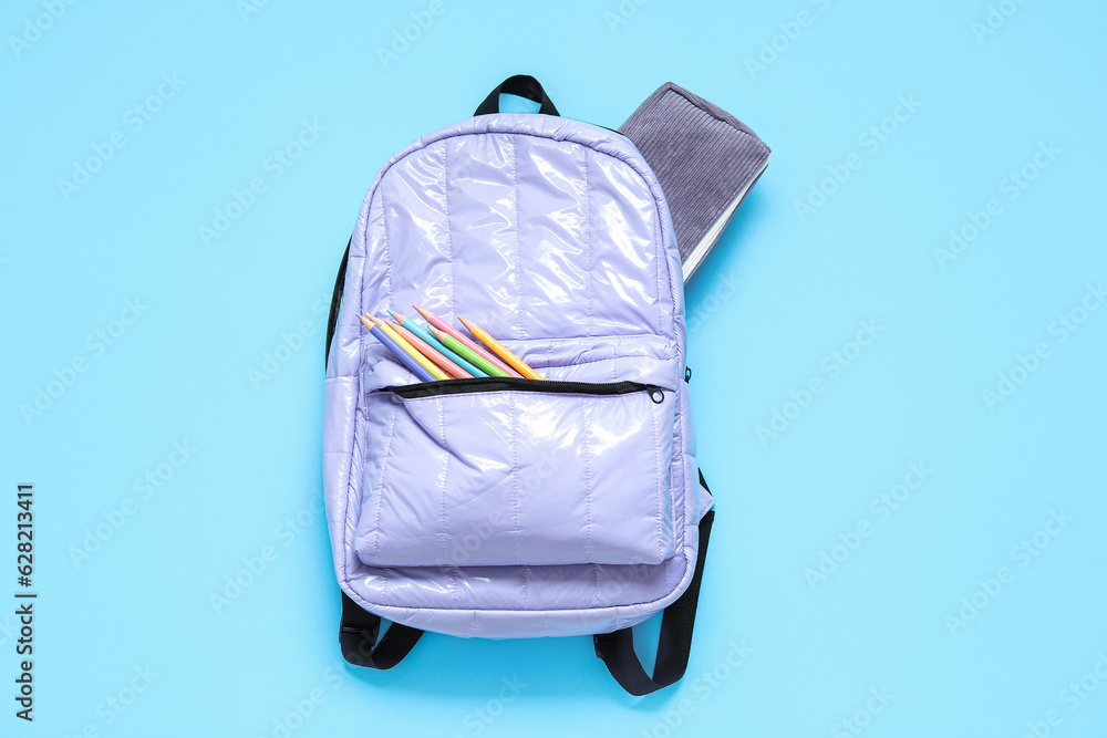 Lilac school backpack with stationery on blue background