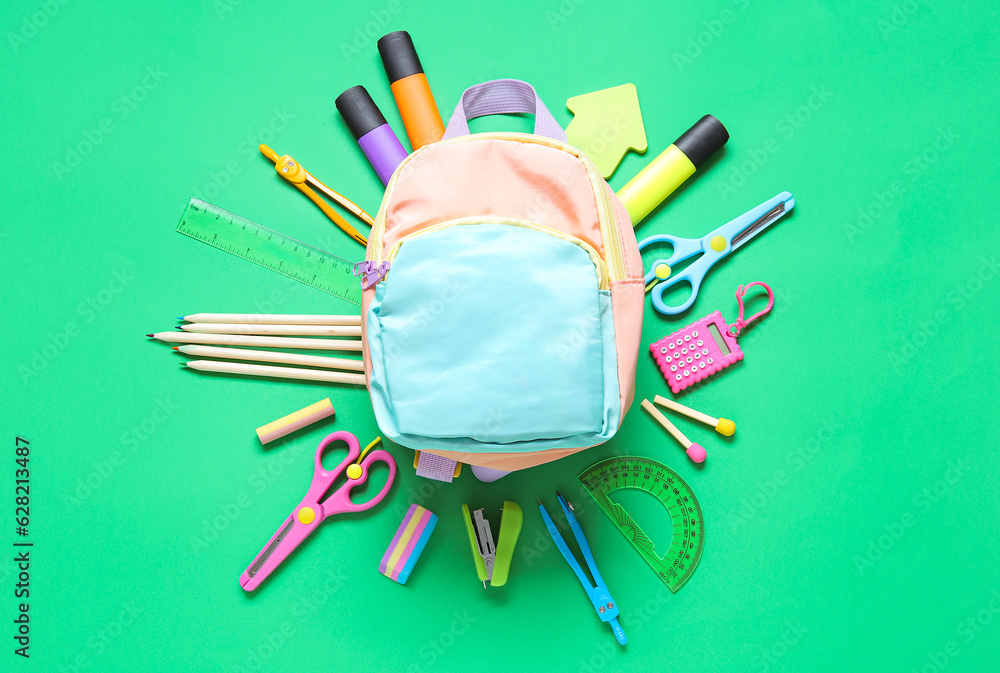 Color school backpack with different stationery on green background