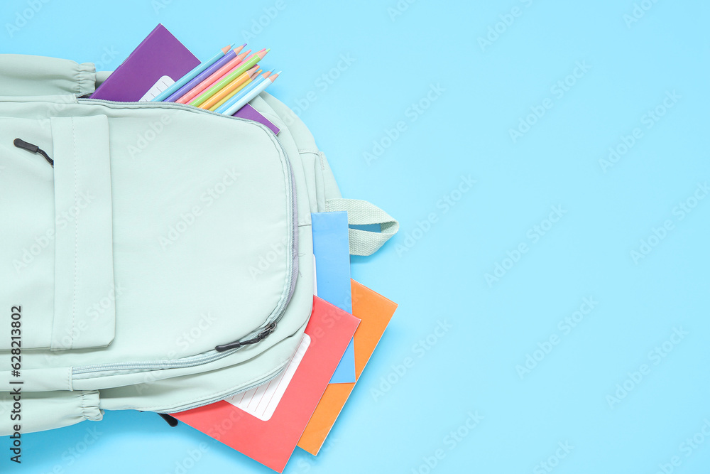 Green school backpack with stationery on blue background