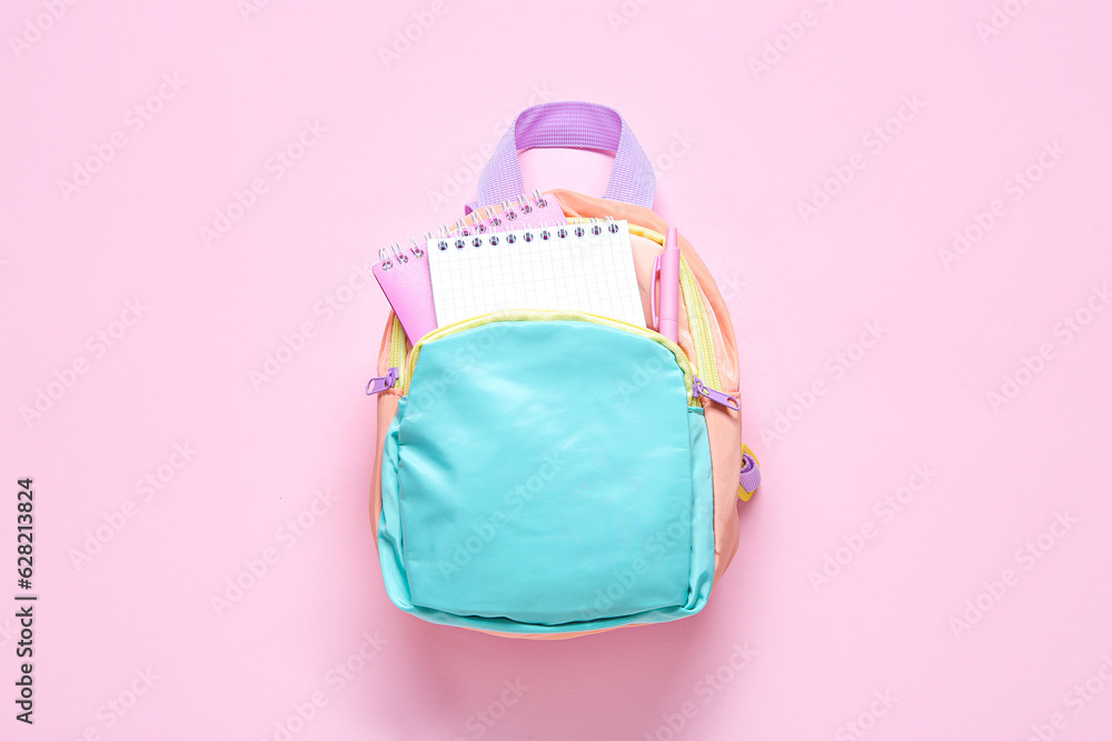 Color school backpack with stationery on pink background