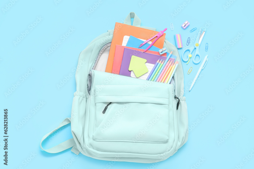 Green school backpack with different stationery on blue background