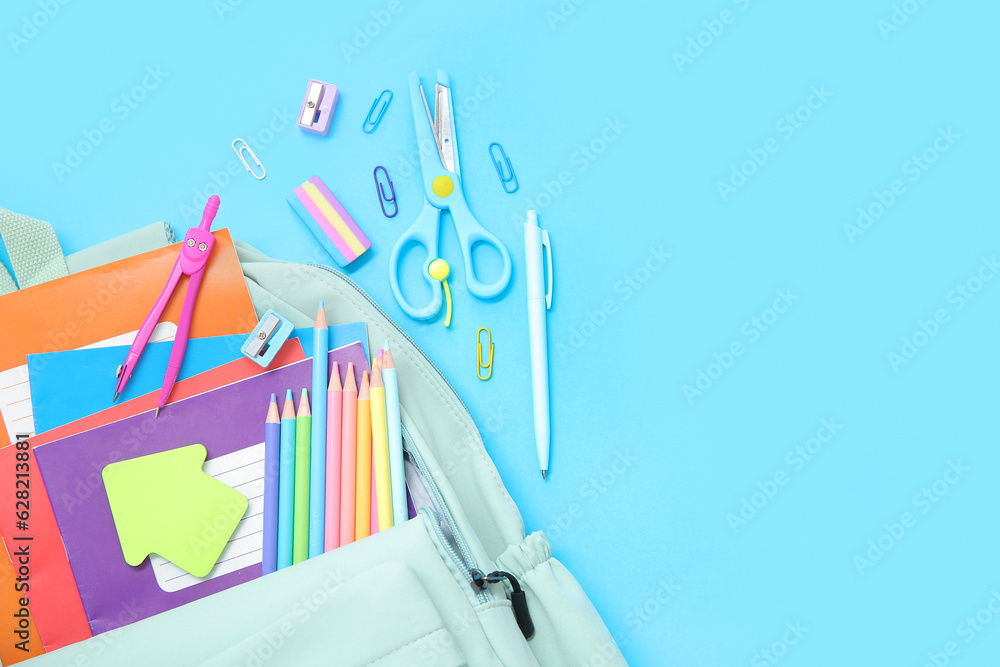 Green school backpack with different stationery on blue background