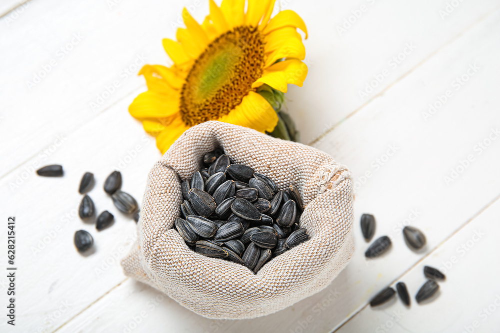 Beautiful sunflower and sack bag with seeds on white wooden background