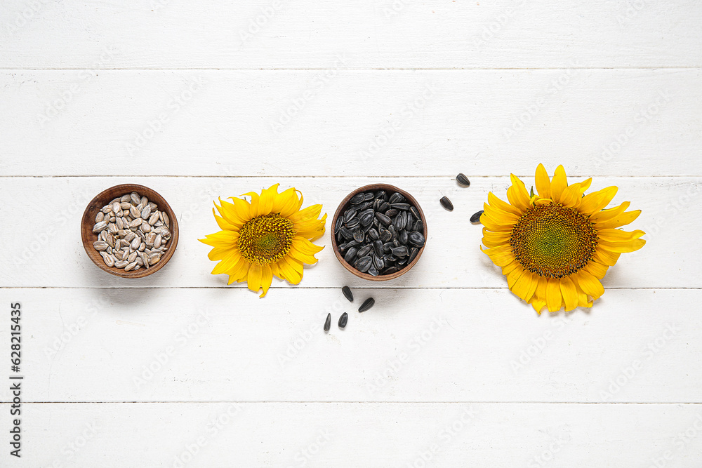 Beautiful sunflowers and bowls with seeds on white wooden background