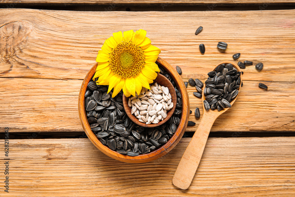 Beautiful sunflower and bowls with seeds on wooden background