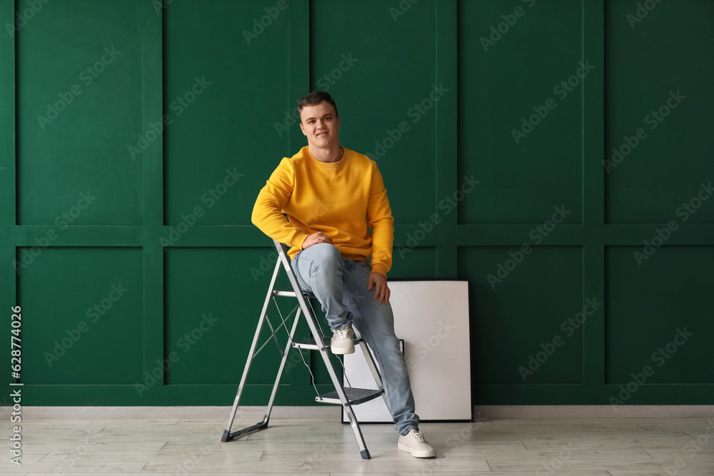 Young man sitting on ladder near green wall