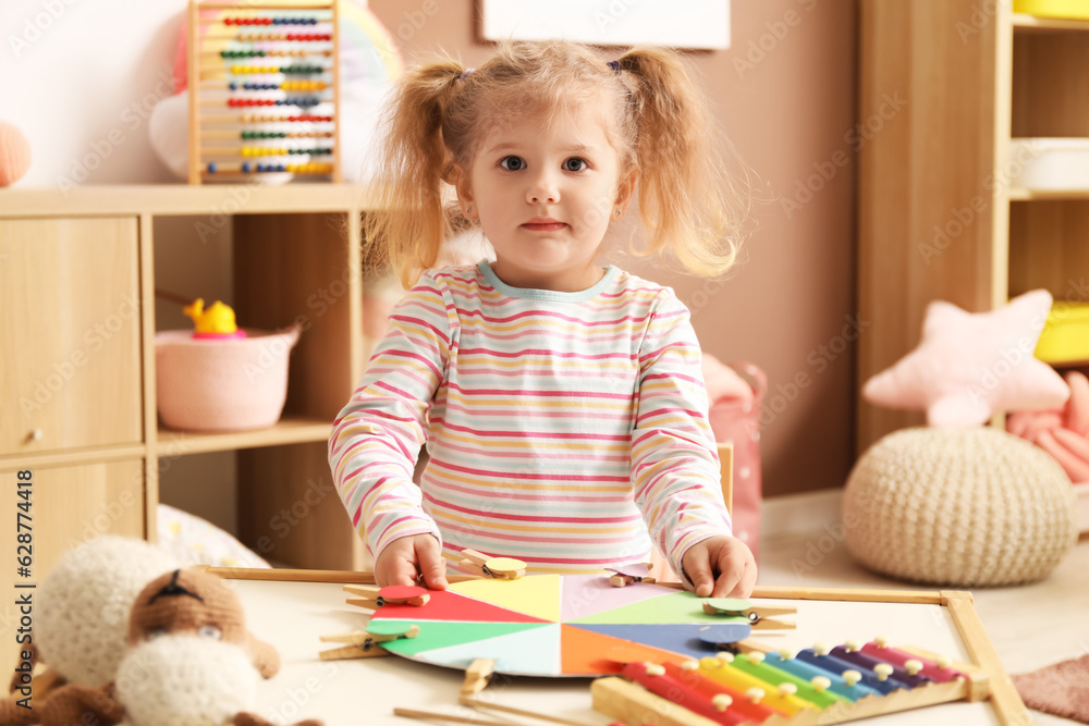 Cute little girl playing matching game with clothespins at home