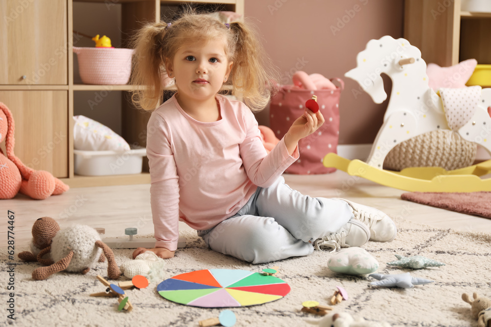 Cute little girl playing matching game with clothespins on floor at home