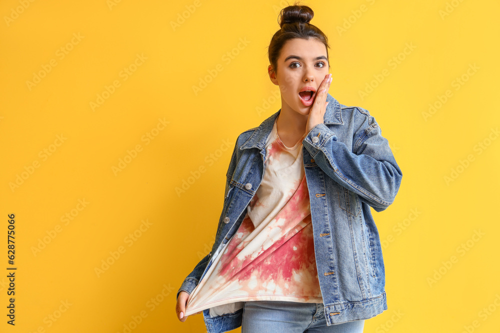 Surprised young woman in tie-dye t-shirt on yellow background