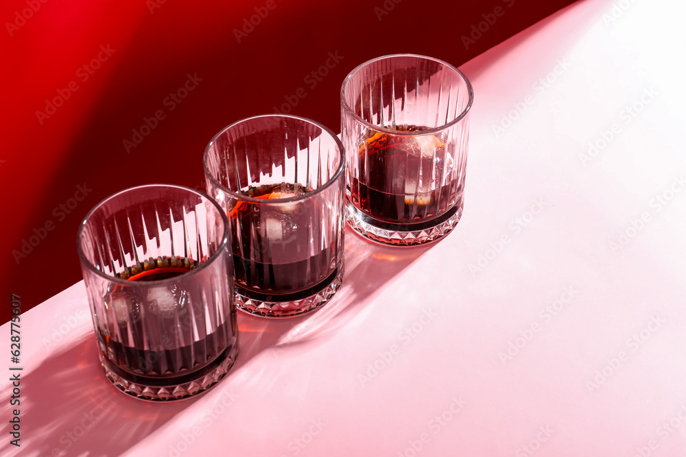 Glasses of rum with ice cubes on pink background