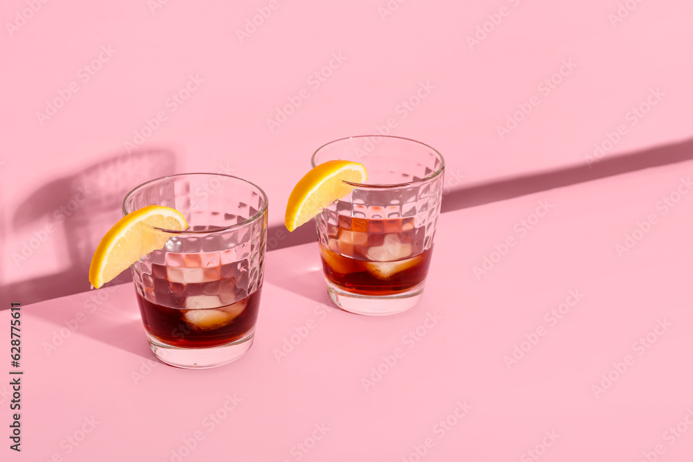 Glasses of rum with ice cubes and lemon slices on pink background