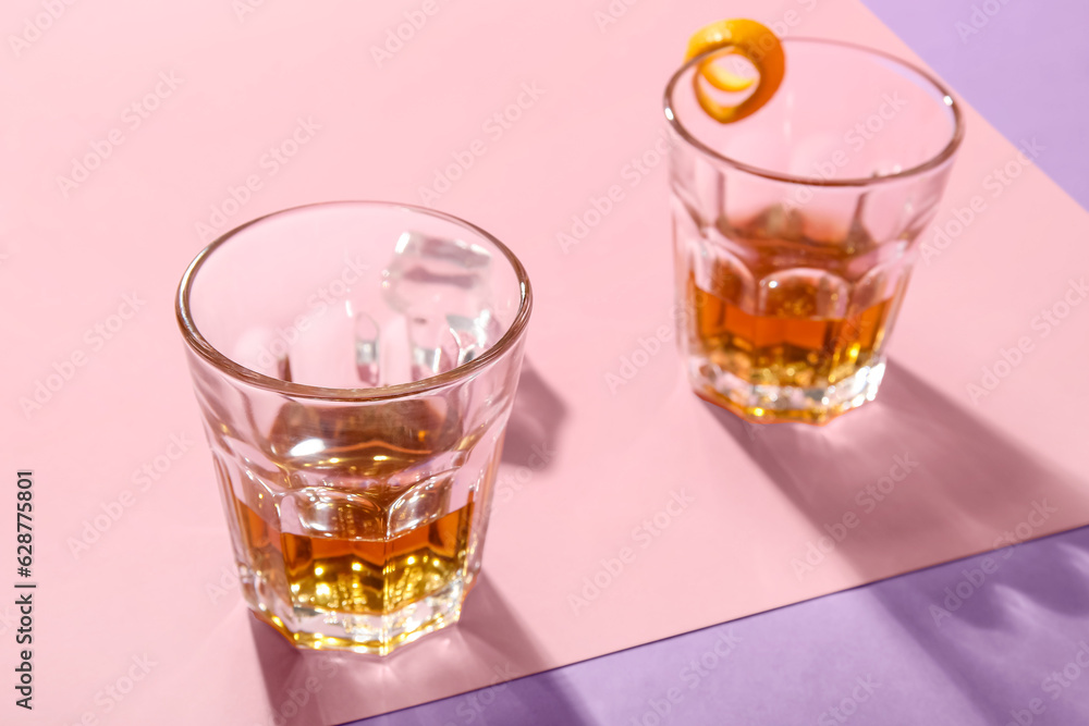 Glasses with rum, ice cubes and orange peels on colorful background