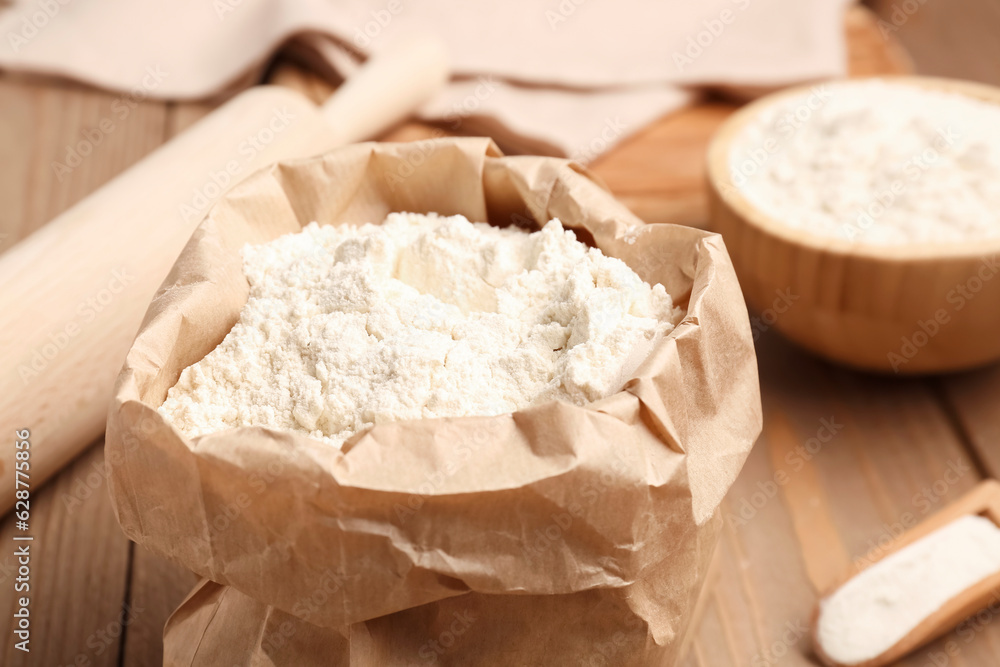 Paper bag with wheat flour on wooden table, closeup