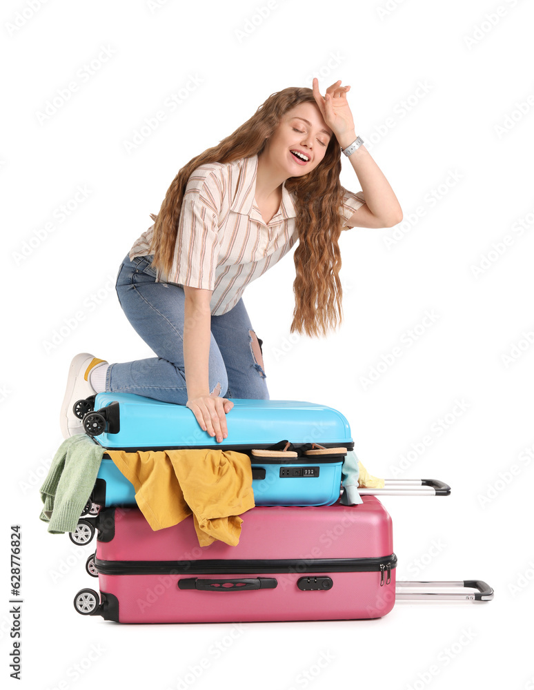 Tired young woman trying to close suitcase with a lot of things on white background