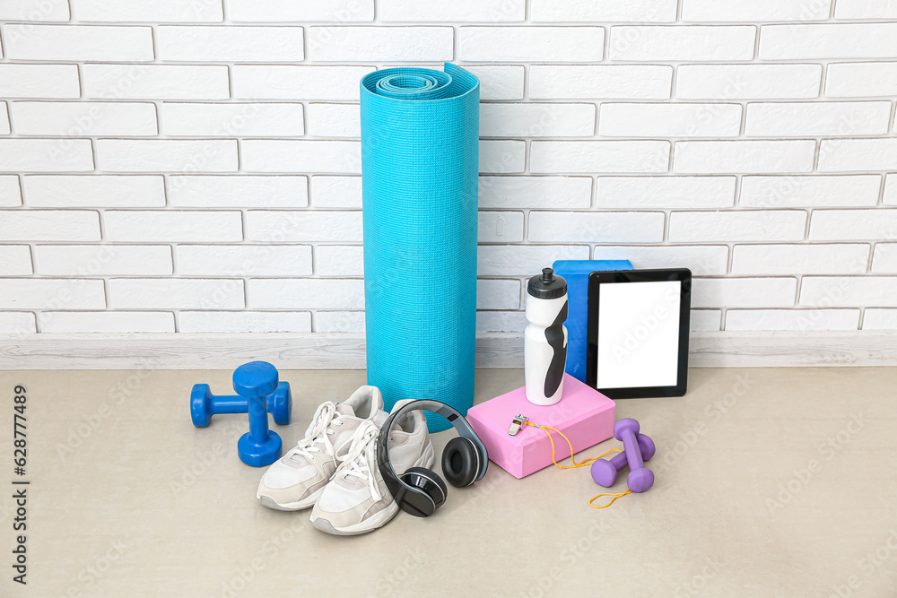 Sports equipment with headphones, tablet computer and bottle near white brick wall