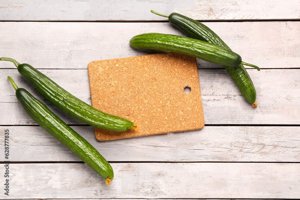 Board with fresh cucumber on light wooden background