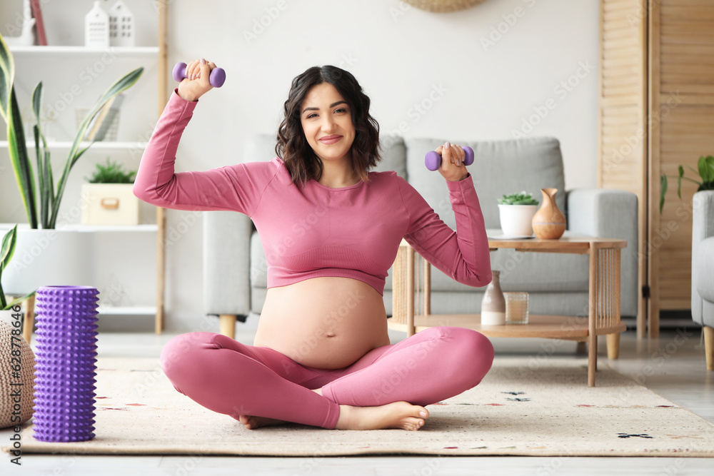 Sporty pregnant woman training with dumbbells at home