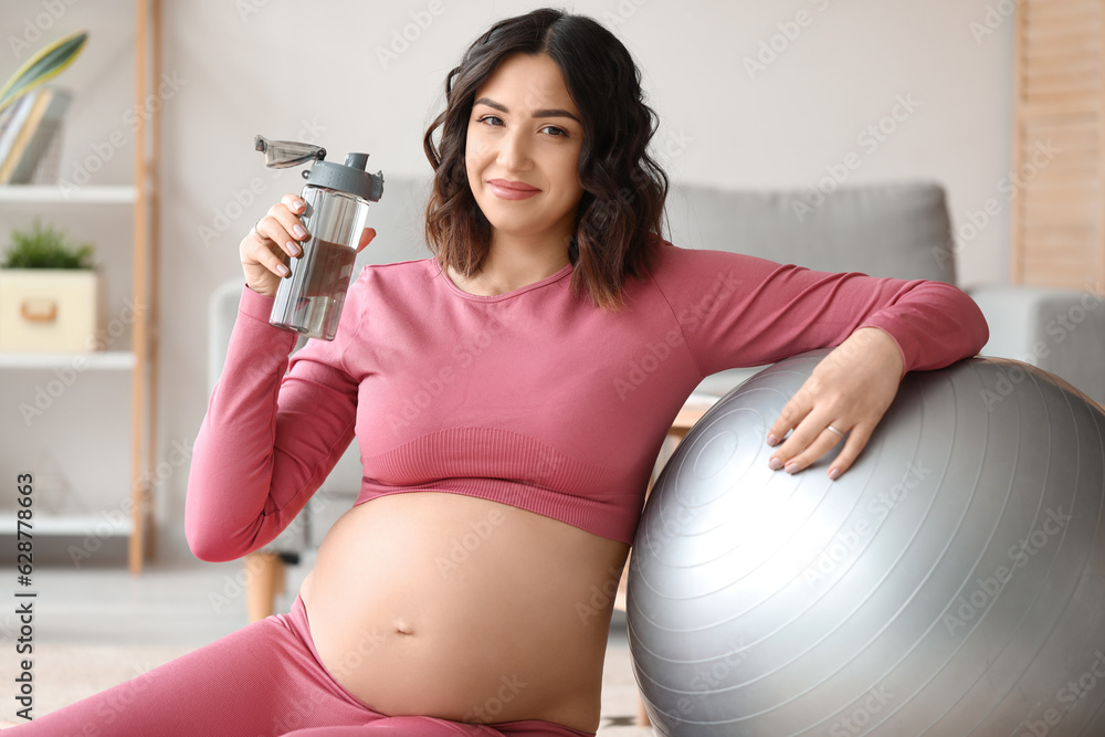 Sporty pregnant woman with bottle of water and fitball at home