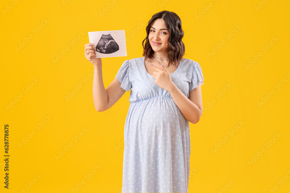 Young pregnant woman pointing at sonogram image on yellow background