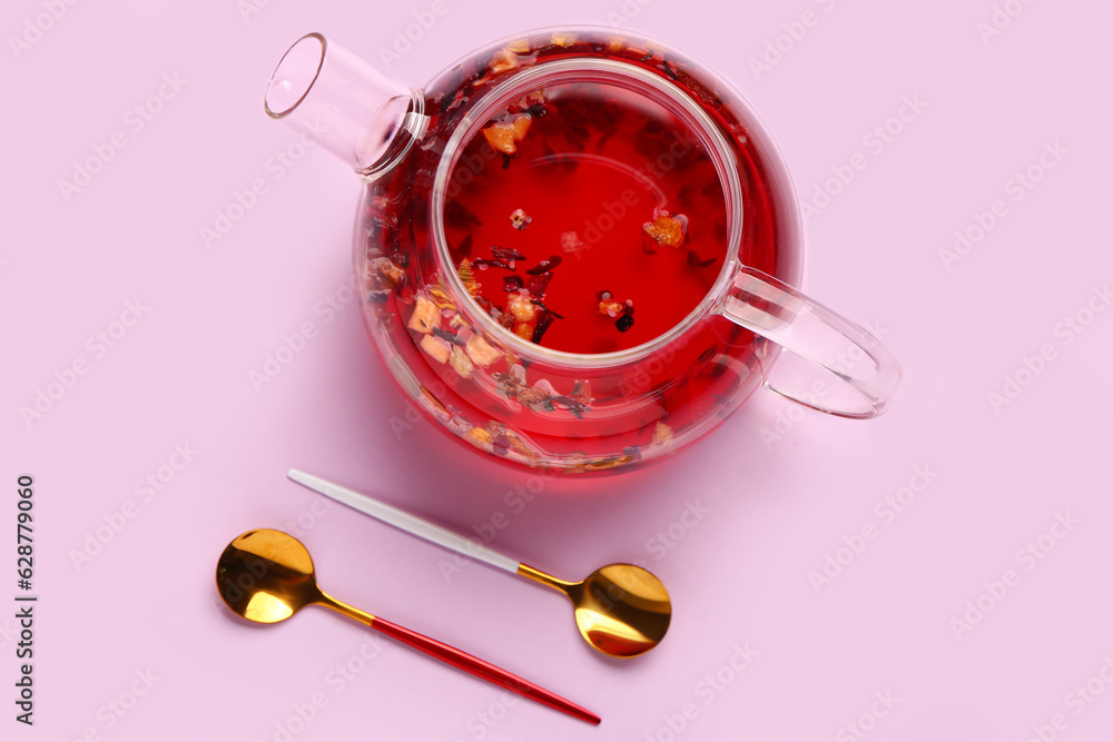 Transparent teapot with spoons on lilac background