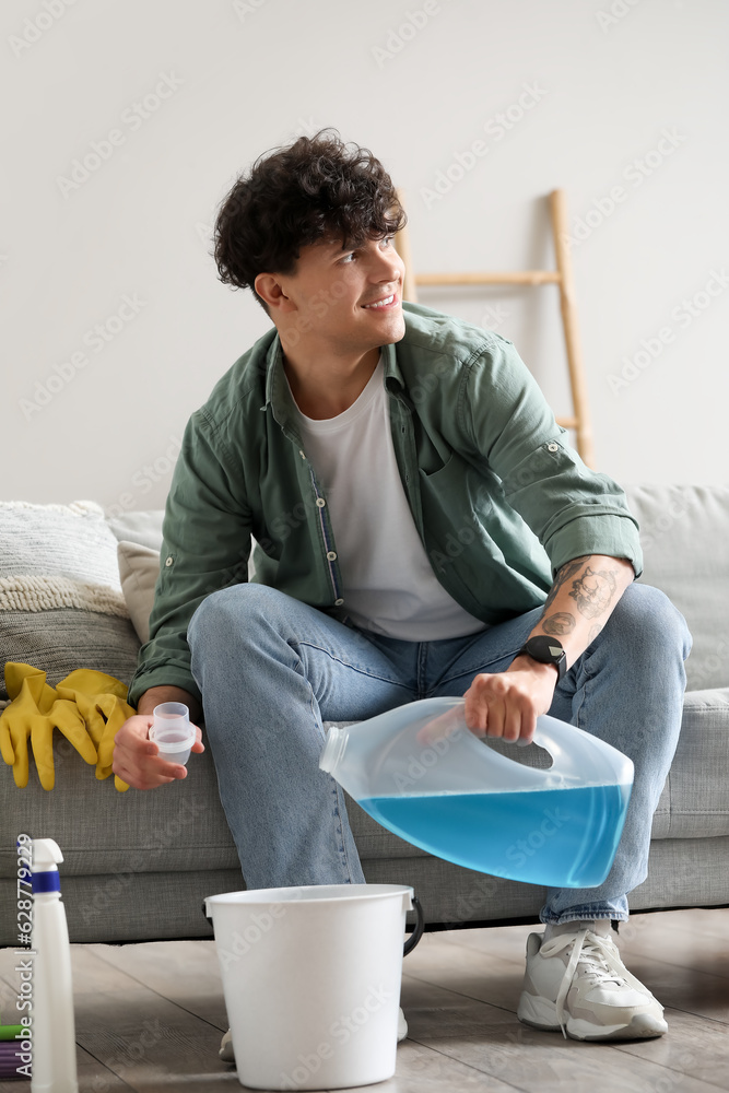 Young man pouring detergent into bucket at home