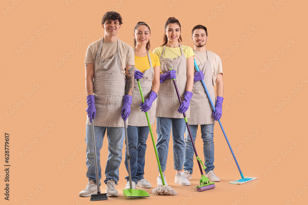 Young janitors with cleaning supplies on beige background