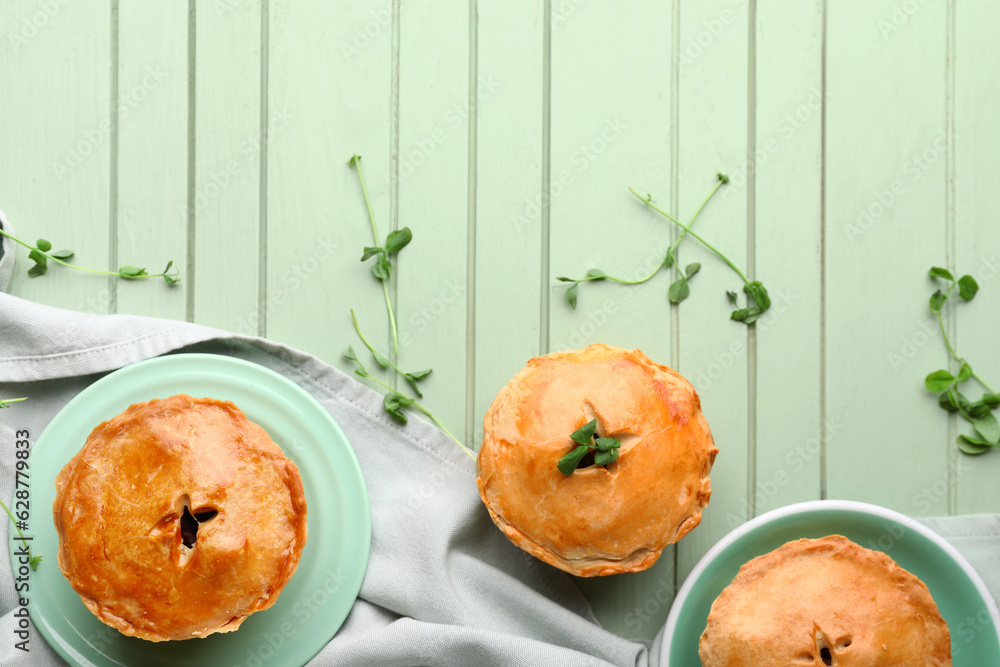 Plates with tasty meat pot pie on green wooden background