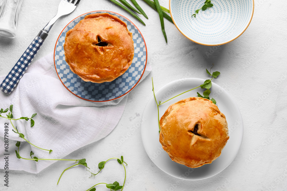 Plates with tasty meat pot pies on light background