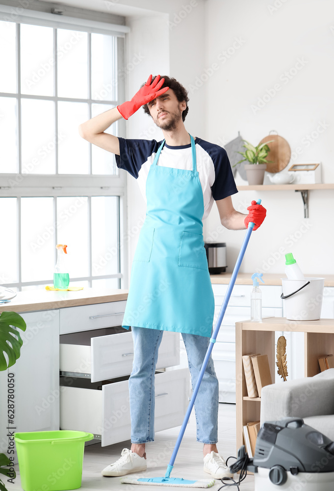 Tired young man mopping floor in kitchen