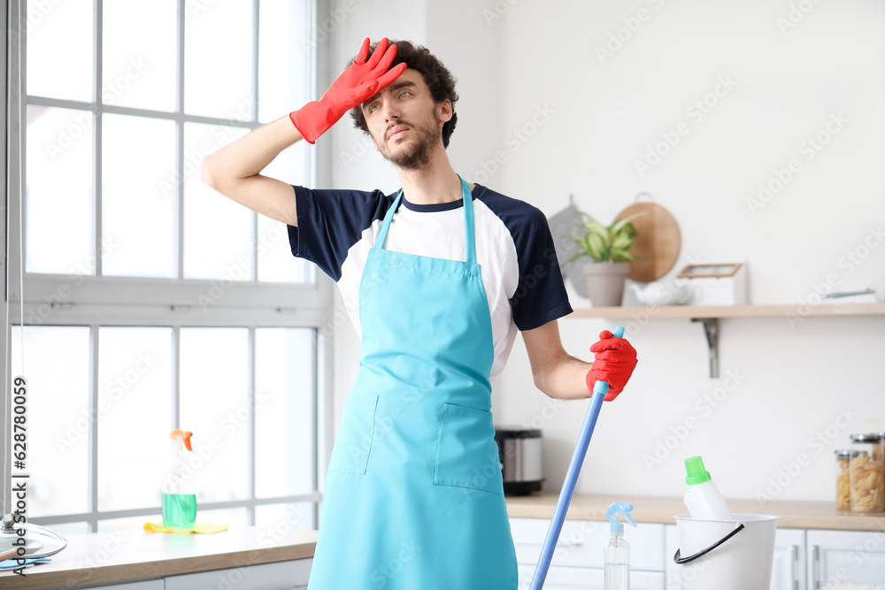 Tired young man mopping floor in kitchen