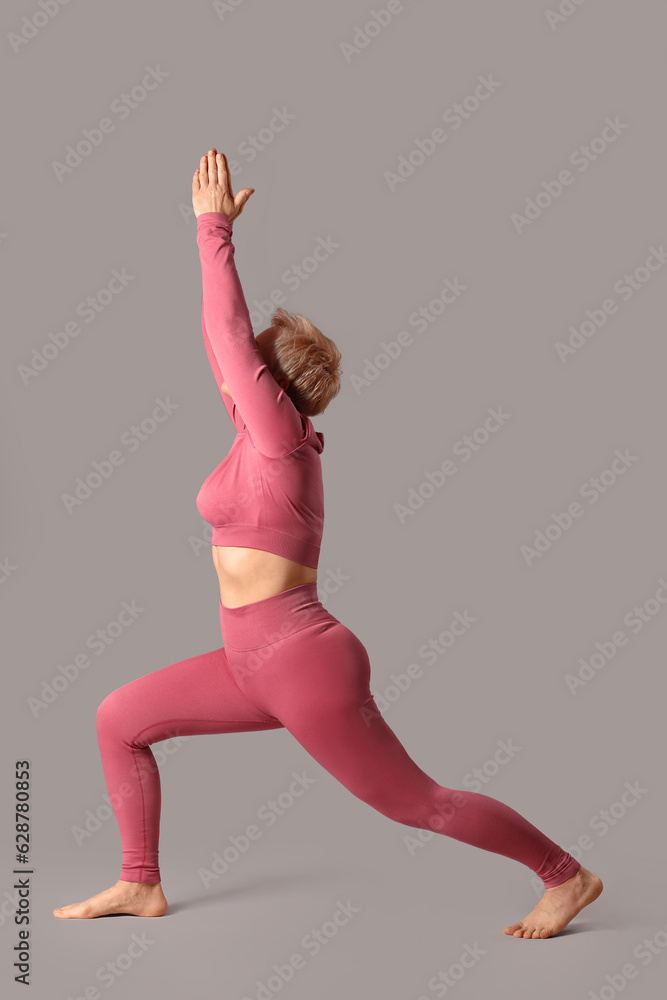 Sporty mature woman practicing yoga on grey background