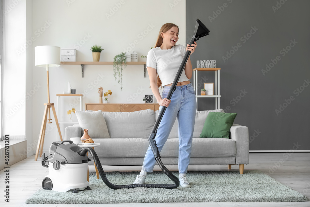 Young woman with vacuum cleaner singing at home