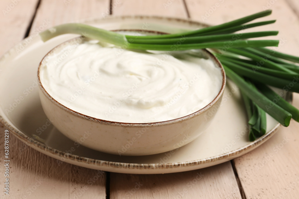 Bowl of tasty sour cream with green onion on light wooden background