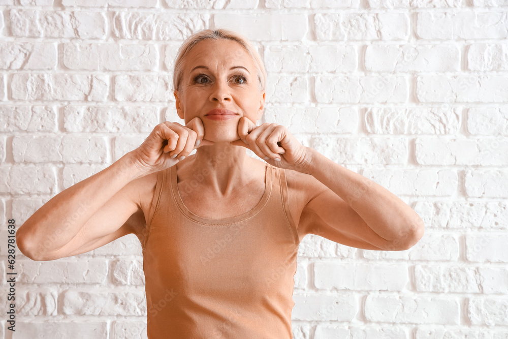 Mature woman doing face building exercise on white brick background