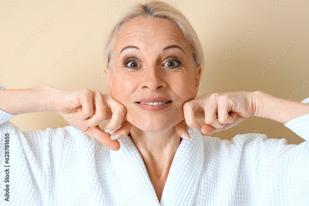 Mature woman doing face building exercise on beige background, closeup