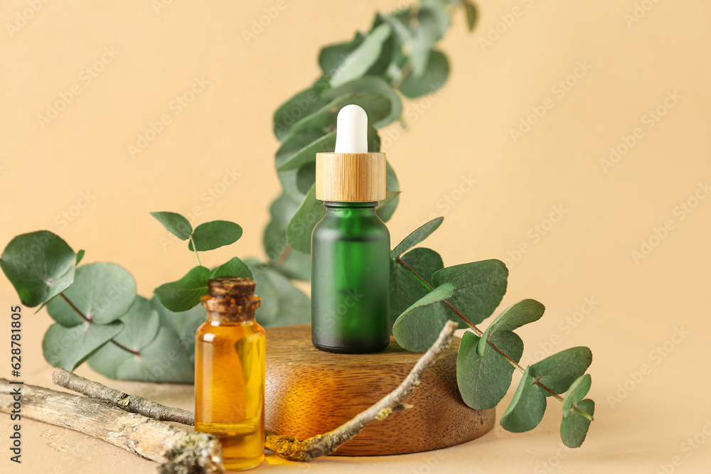 Bottles of cosmetic oil with eucalyptus branch on orange background