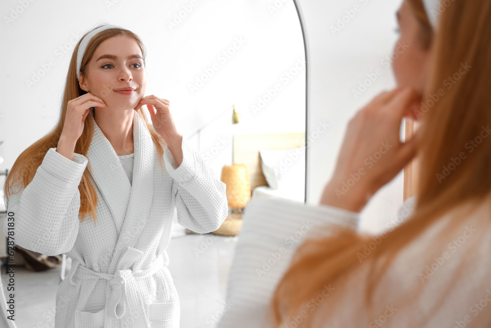 Young woman doing face building exercise near mirror in bathroom