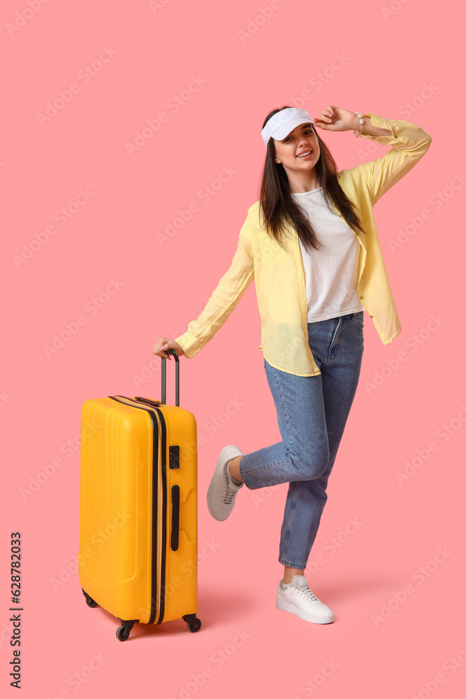 Young woman with suitcase on pink background