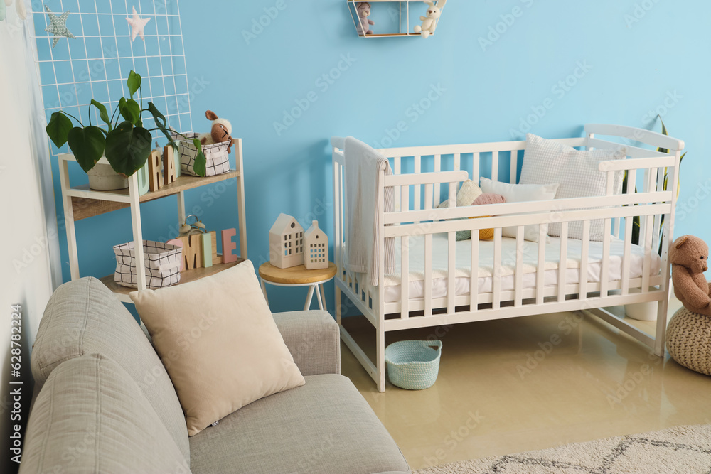 Interior of stylish bedroom with baby crib, sofa and shelving unit