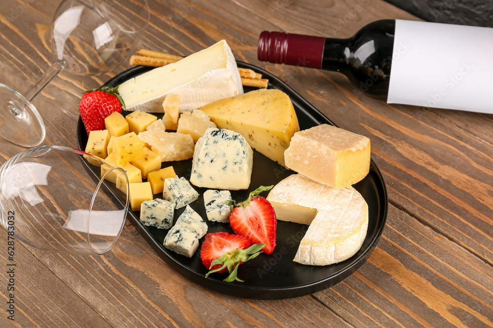 Pieces of tasty cheese, glasses and bottle with wine on wooden background