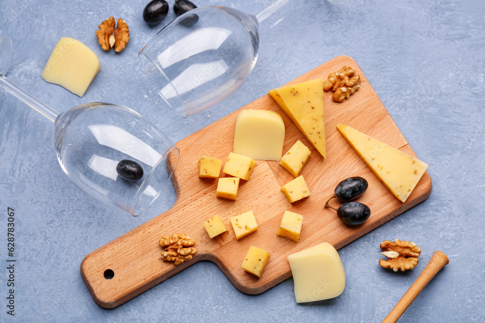 Wooden board with pieces of tasty cheese and wine glasses on grey background