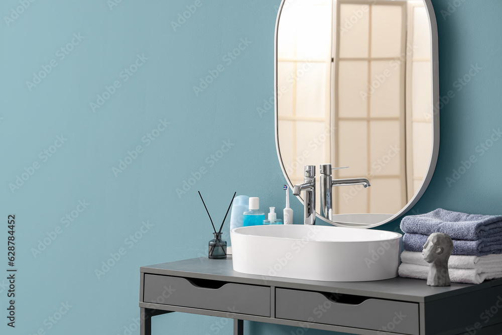 White sink with bath accessories on table near color wall